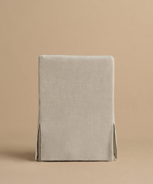 The Sunset Dining Arm Chair in beige linen features a straight back and tailored skirt, shown against a plain beige background. The chair faces forward, highlighting its simple, modern California style.