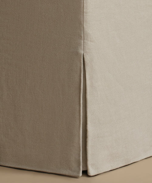 Close-up of a beige upholstered furniture corner with a skirted edge and visible fabric texture.