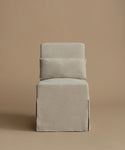 An accent chair upholstered in a textured light gray fabric, featuring a tiered backrest with two rectangular cushions, set against a solid warm beige background.