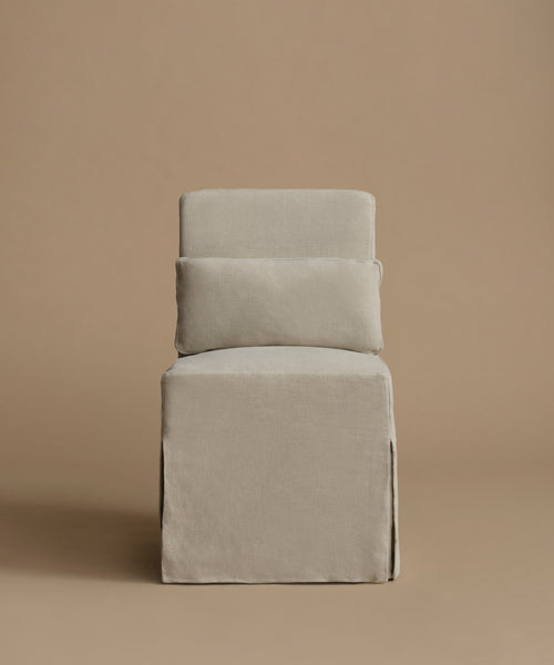 An accent chair upholstered in a textured light gray fabric, featuring a tiered backrest with two rectangular cushions, set against a solid warm beige background.