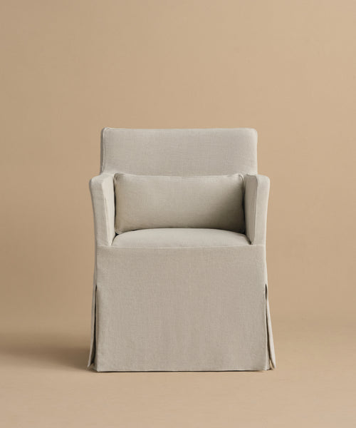 The Sunset Dining Arm Chair features a straight back, matching rectangular cushion, and skirted base in beige linen, capturing California design elegance against a plain beige background.