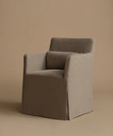 An armchair upholstered in a textured taupe fabric, featuring a high back, wide armrests, and a skirted base, set against a solid warm beige studio background.