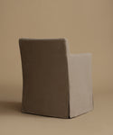 A single upholstered dining chair shown from the back in a studio setting, with a dark taupe backrest and a light beige side panel on a warm beige background.