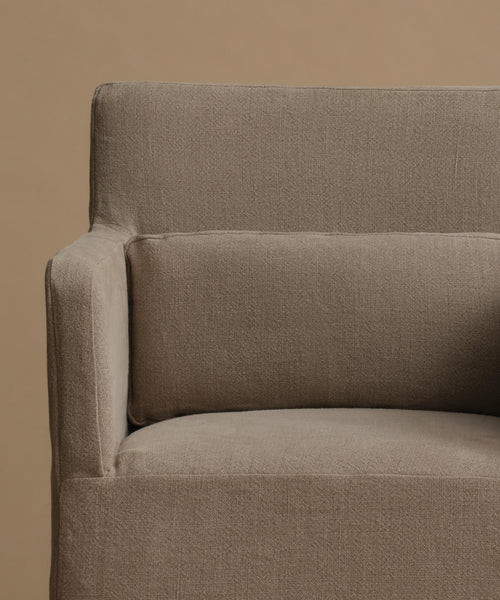 Close-up of a textured taupe fabric armchair with a matching back cushion against a solid beige background.