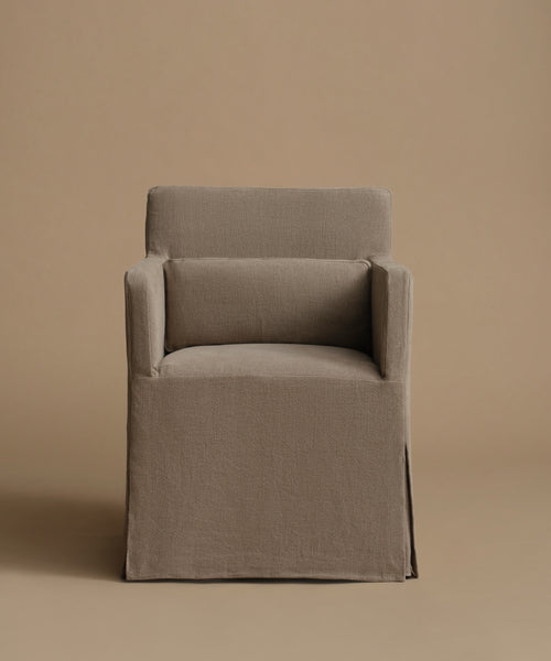 A slipcovered armchair upholstered in a textured taupe linen fabric, set against a solid warm beige studio background.