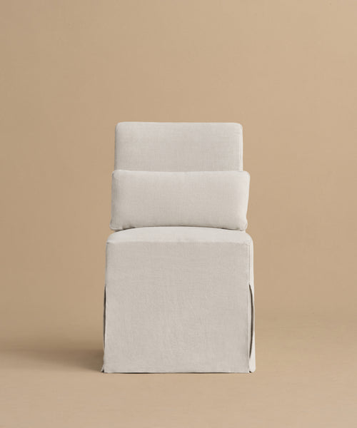 The Sunset Dining Chair features a modern, minimalist California design with clean lines and a light gray upholstered seat, backrest, and base. Its boxy geometric shape is set against a plain beige background for a soft, elegant look.