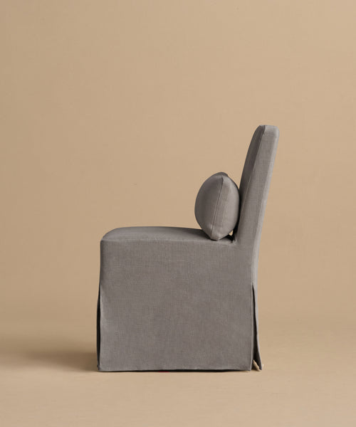 The Sunset Dining Chair features gray upholstery, a straight back, and a round lumbar pillow, pictured in profile against a plain beige background.
