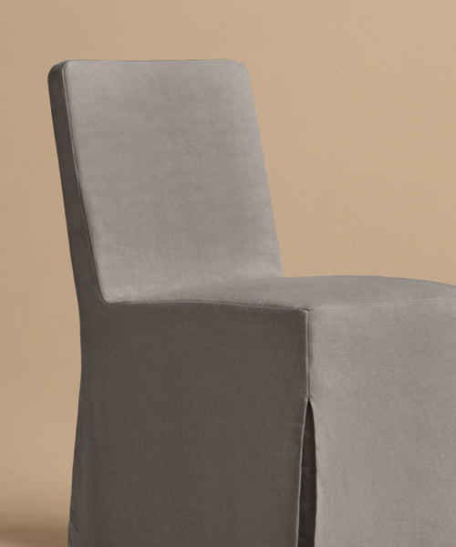 The Sunset Dining Chair features a modern, armless design with a high back and straight lines, upholstered in smooth gray linen that showcases California style. Displayed against a simple beige background.