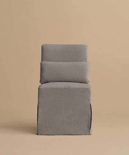 The Sunset Dining Chair, featuring a straight backrest and seat upholstered in light gray fabric, showcases modern California style against a plain beige background.