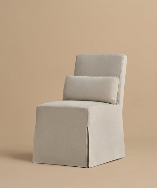 The Sunset Dining Chair is a modern, armless seat with light beige fabric, square backrest, removable slipcover, and matching rectangular lumbar cushion, shown against a plain taupe background.