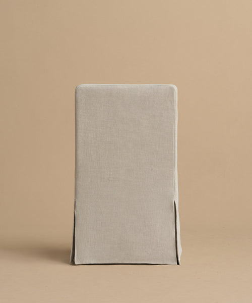 The Sunset Dining Chair, featuring a light beige linen removable slipcover with two front corner slits, is shown against a plain beige background.