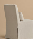 The Sunset Dining Chair is a modern, armless seat with a high back and light beige linen upholstery, shown angled left on a solid tan background.