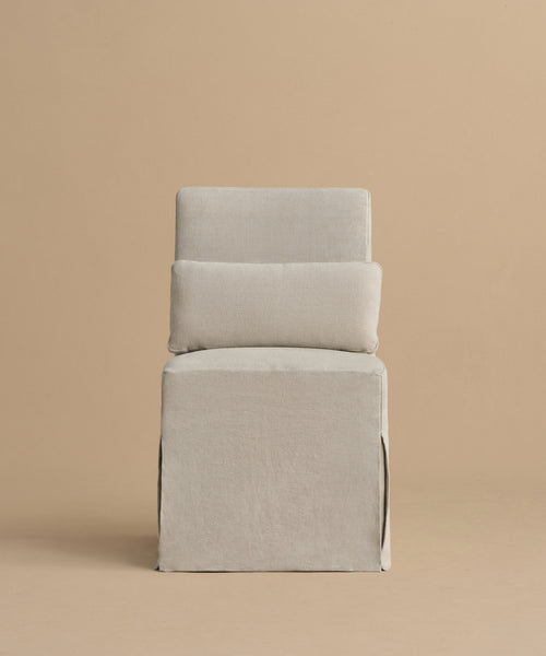 The Sunset Dining Chair is a minimalist, modern piece with light beige linen upholstery, a boxy base, rectangular backrest, and a matching cushion with removable slipcover, shown against a plain beige background.