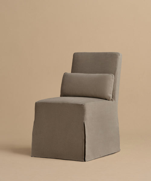 The Sunset Dining Chair is a modern, armless taupe linen chair with a fabric slipcover, straight back, clean lines, and a rectangular lumbar cushion, shown on a neutral background.