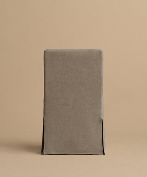 The Sunset Dining Chair features a rectangular taupe linen design with a fitted slipcover, tailored seams, and side slits, shown on a beige background.