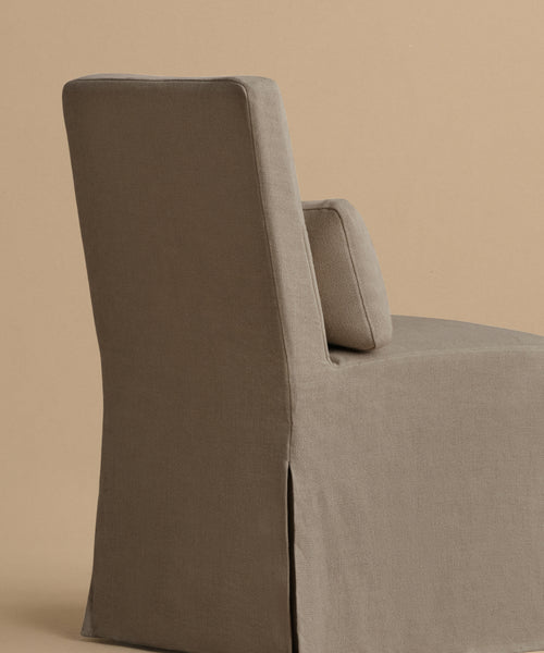 The Sunset Dining Chair features taupe linen upholstery, a squared backrest, and a matching cushion, shown from the side against a beige background—offering a chic, modern look for any dining space.