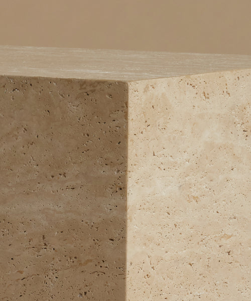A close-up of a travertine stone coffee table showing its natural beige and cream porous texture under warm, soft lighting.