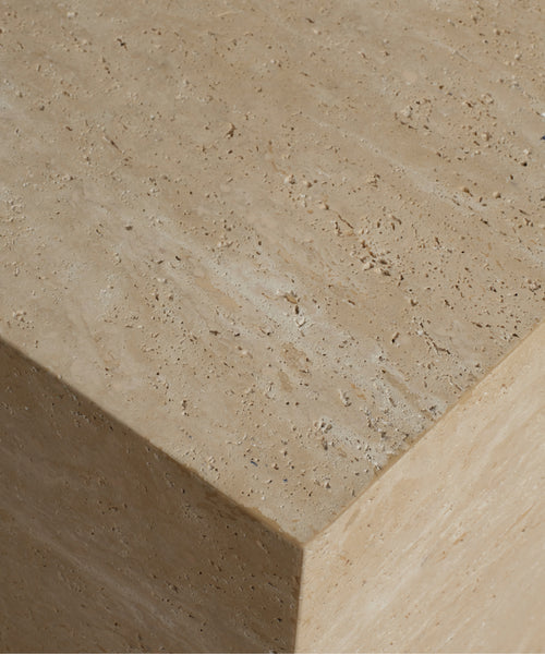 Close-up of a beige travertine stone surface with natural pitting texture and a visible corner edge.