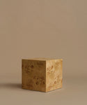 A square burl wood side table standing upright on a beige surface against a solid beige background.