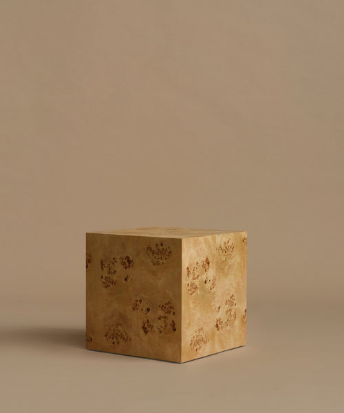 A square burl wood side table standing upright on a beige surface against a solid beige background.