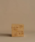 A square burl wood side table standing upright on a beige surface against a solid beige background.
