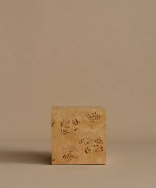 A square burl wood side table standing upright on a beige surface against a solid beige background.