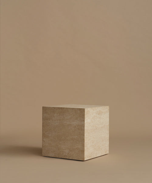 A square travertine side table, standing upright on a matching beige surface against a solid beige background.