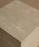 A close-up of a beige travertine stone side table showing its natural porous texture and layered surface details against a matching neutral background.