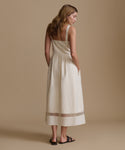Woman wearing an ivory dress and sandals against a beige backdrop.