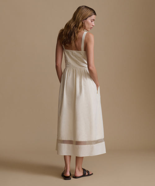 Woman wearing an ivory dress and sandals against a beige backdrop.
