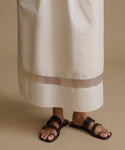 Woman wearing an ivory dress and sandals against a beige backdrop.