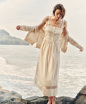 Woman wearing an ivory dress and cardigan at the beach.