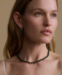 Woman wearing a green beaded necklace and earrings against a beige background