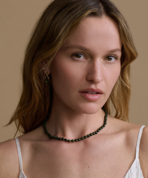 Woman wearing a green beaded necklace against a beige background