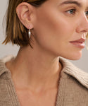 A close-up of a woman with short light brown hair wearing a beige knit sweater and a single Tiny Spear Hoop earring, looking to the right.