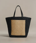 The Tropez Tote Bag is a handcrafted summer accessory from Tuscany, highlighting black woven material, dual handles, and a large light cane webbing panel on the front, showcased against a neutral backdrop.
