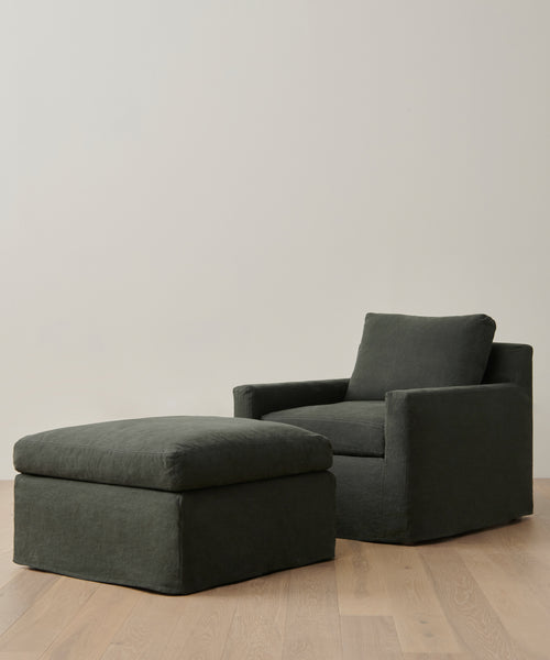 A dark green upholstered armchair with a matching Harbor Ottoman from Jenni Kayne Furniture sits on a light wooden floor against a plain, light-colored wall.