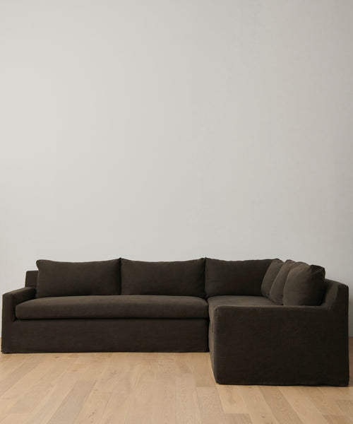 A modern Harbor Sectional in dark brown, featuring clean lines, sits on light wood flooring against a white wall, highlighting the timeless elegance of Jenni Kayne Furniture.