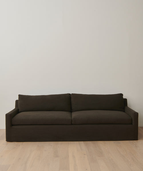 The Harbor Sofa features dark brown linen upholstery, straight arms, and two seat and back cushions; it sits against an off-white wall on light wood flooring.