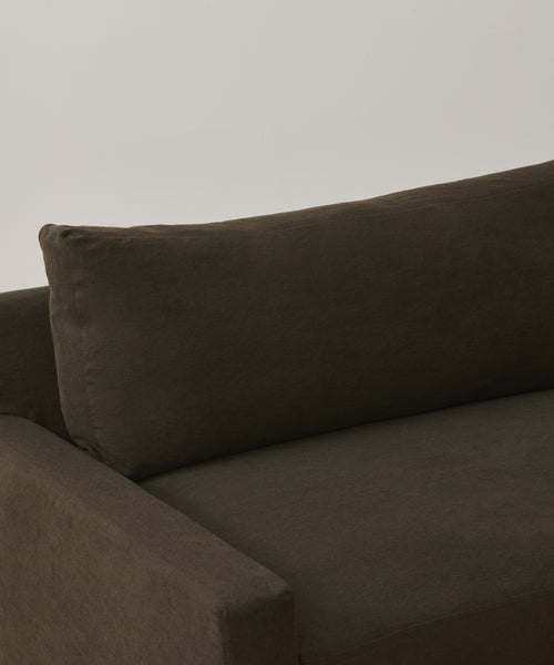 A close-up of the Harbor Sofa, featuring modern design in dark brown linen upholstery with visible armrest, seat cushion, and backrest set against a plain, light-colored wall.