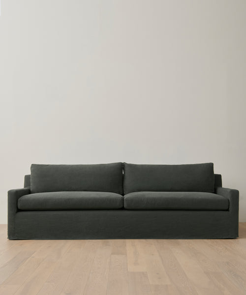 The Harbor Sofa is a modern piece in dark gray linen, featuring two seat and two back cushions. It’s shown against a light wall and set on a light wood floor.