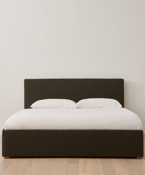 The Pacific Bed Warehouse Sale offers a modern bed with a dark upholstered headboard and frame, white bedding and pillows, all set on a light wooden floor—an ideal choice for updating any contemporary bedroom.