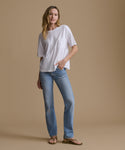 A woman modeling a white short-sleeve pocket T-shirt and light-wash blue jeans against a solid beige studio background.
