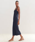 A woman smiles sideways in an ankle-length, sleeveless Rib Tank Dress in dark navy with tan strappy flats—a perfect warm-weather staple—set against a plain light background.