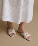 White sandals worn with a white skirt on a beige background
