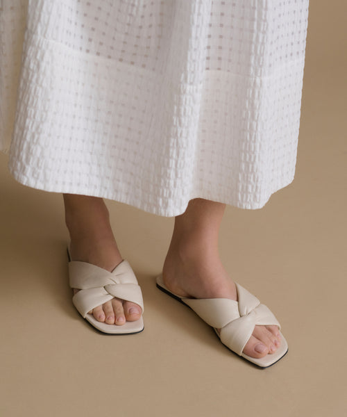 White sandals worn with a white skirt on a beige background
