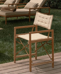 Wooden chair with beige cushion on a wooden deck with grass in the background