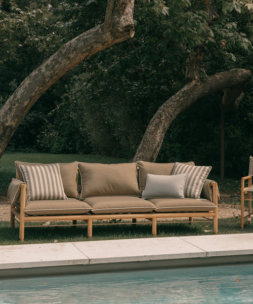 Outdoor sofa with cushions by a poolside in a garden setting