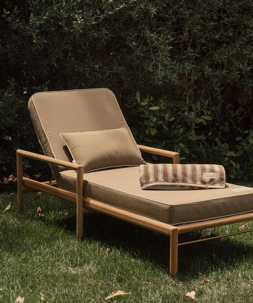 Beige outdoor lounge chair with cushions on a grassy area with greenery in the background