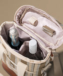Open beige travel bag with a bottle and other items on a neutral background